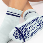 Women wearing a light sky blue ankle grip sock with navy blue stripes on the toes and top ankle cuff made for Pilates, Barre, Yoga, and beyond. 