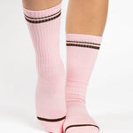Women wearing a baby pink crew grip sock with dark brown stripes on the toes and top ankle cuff made for Pilates, Barre, Yoga, and beyond. 