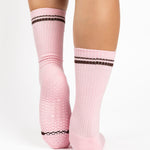 Women wearing a baby pink crew grip sock with dark brown stripes on the toes and top ankle cuff made for Pilates, Barre, Yoga, and beyond. 