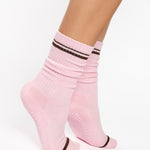 Women wearing a baby pink crew grip sock with dark brown stripes on the toes and top ankle cuff made for Pilates, Barre, Yoga, and beyond. 