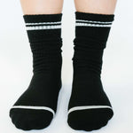 Women wearing a solid black crew grip sock with white stripes on the toes and top ankle cuff made for Pilates, Barre, Yoga, and beyond. 
