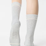 Women wearing a heather grey crew grip sock with white stripes on the toes and top ankle cuff made for Pilates, Barre, Yoga, and beyond. 