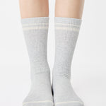 Women wearing a heather grey crew grip sock with white stripes on the toes and top ankle cuff made for Pilates, Barre, Yoga, and beyond. 
