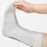 Women wearing a heather grey crew grip sock with white stripes on the toes and top ankle cuff made for Pilates, Barre, Yoga, and beyond. 