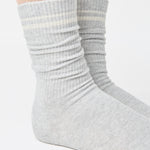 Women wearing a heather grey crew grip sock with white stripes on the toes and top ankle cuff made for Pilates, Barre, Yoga, and beyond. 