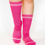 Women wearing a solid hot pink crew grip sock with white stripes on the toes and top ankle cuff made for Pilates, Barre, Yoga, and beyond. 