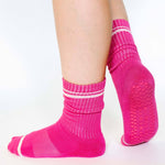 Women wearing a solid hot pink crew grip sock with white stripes on the toes and top ankle cuff made for Pilates, Barre, Yoga, and beyond. 