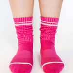 Women wearing a solid hot pink crew grip sock with white stripes on the toes and top ankle cuff made for Pilates, Barre, Yoga, and beyond. 