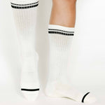 Women wearing a solid white crew grip sock with black stripes on the toes and top ankle cuff made for Pilates, Barre, Yoga, and beyond. 