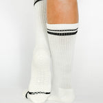 Women wearing a solid white crew grip sock with black stripes on the toes and top ankle cuff made for Pilates, Barre, Yoga, and beyond. 