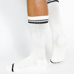 Women wearing a solid white crew grip sock with black stripes on the toes and top ankle cuff made for Pilates, Barre, Yoga, and beyond. 