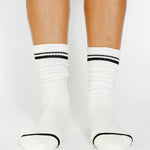 Women wearing a solid white crew grip sock with black stripes on the toes and top ankle cuff made for Pilates, Barre, Yoga, and beyond. 