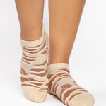 Woman wearing a tan full foot grip sock with brown animal print, made for pilates, barre, yoga, and beyond.  