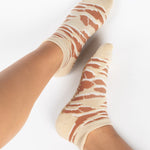 Woman wearing a tan full foot grip sock with brown animal print, made for pilates, barre, yoga, and beyond.  