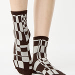 Women wearing an ankle grip sock with a dark brown and grey checkered design, made for pilates, barre, yoga, and beyond.