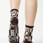 Women wearing an ankle grip sock with a dark brown and grey checkered design, made for pilates, barre, yoga, and beyond.