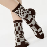 Women wearing an ankle grip sock with a dark brown and grey checkered design, made for pilates, barre, yoga, and beyond.