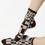 Women wearing an ankle grip sock with a dark brown and grey checkered design, made for pilates, barre, yoga, and beyond.