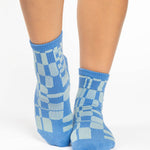 Women wearing an ankle grip sock with a sky blue and light blue checkered design, made for pilates, barre, yoga, and beyond.