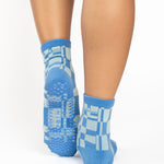 Women wearing an ankle grip sock with a sky blue and light blue checkered design, made for pilates, barre, yoga, and beyond.