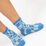 Women wearing an ankle grip sock with a sky blue and light blue checkered design, made for pilates, barre, yoga, and beyond.