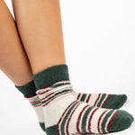 Woman wearing festive white with green and red striped crew ultra plush soft grip socks made for recovery, post pilates, barre, yoga, and beyond.