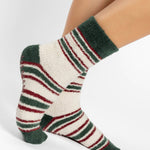 Woman wearing festive white with green and red striped crew ultra plush soft grip socks made for recovery, post pilates, barre, yoga, and beyond.