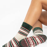 Woman wearing festive white with green and red striped crew ultra plush soft grip socks made for recovery, post pilates, barre, yoga, and beyond.