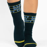 Woman wearing a black crew grip sock with "Sanity Not Vanity" written on the top cuff area in blue, made for pilates, barre, yoga, and beyond.