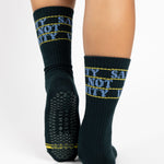 Woman wearing a black crew grip sock with "Sanity Not Vanity" written on the top cuff area in blue, made for pilates, barre, yoga, and beyond.