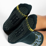 Woman wearing a black crew grip sock with "Sanity Not Vanity" written on the top cuff area in blue, made for pilates, barre, yoga, and beyond.