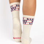 Woman wearing an off white crew grip sock with "Sanity Not Vanity" written on the top cuff area in blue, made for pilates, barre, yoga, and beyond.