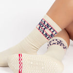 Woman wearing an off white crew grip sock with "Sanity Not Vanity" written on the top cuff area in blue, made for pilates, barre, yoga, and beyond.