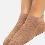 Woman wearing a tan full foot grip sock with a raised macaroni terry pattern, made for pilates, barre, yoga, and beyond.  
