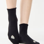Women wearing a black ankle grip sock with a grey heart motif on the top made for Pilates, Barre, Yoga, and beyond. 
