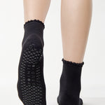 Women wearing a black ankle grip sock with a grey heart motif on the top made for Pilates, Barre, Yoga, and beyond. 
