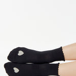 Women wearing a black ankle grip sock with a grey heart motif on the top made for Pilates, Barre, Yoga, and beyond. 