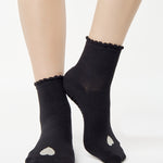 Women wearing a black ankle grip sock with a grey heart motif on the top made for Pilates, Barre, Yoga, and beyond. 