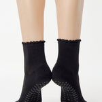 Women wearing a black ankle grip sock with a grey heart motif on the top made for Pilates, Barre, Yoga, and beyond. 
