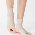 Women wearing a off white ankle grip sock with a red heart motif on the top made for Pilates, Barre, Yoga, and beyond. 