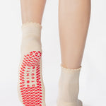 Women wearing a off white ankle grip sock with a red heart motif on the top made for Pilates, Barre, Yoga, and beyond. 