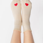 Women wearing a off white ankle grip sock with a red heart motif on the top made for Pilates, Barre, Yoga, and beyond. 