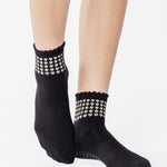 Women wearing a black ankle grip sock with white rows of hearts circling the top ankle made for Pilates, Barre, Yoga, and beyond. 