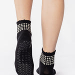 Women wearing a black ankle grip sock with white rows of hearts circling the top ankle made for Pilates, Barre, Yoga, and beyond. 