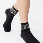 Women wearing a black ankle grip sock with white rows of hearts circling the top ankle made for Pilates, Barre, Yoga, and beyond. 