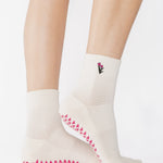 Woman wearing a white ankle grip sock with a tulip motif embroidered on the ankle side, made for pilates, barre, yoga, and beyond. 