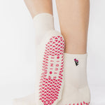 Woman wearing a white ankle grip sock with a tulip motif embroidered on the ankle side, made for pilates, barre, yoga, and beyond. 