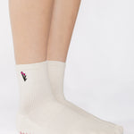 Woman wearing a white ankle grip sock with a tulip motif embroidered on the ankle side, made for pilates, barre, yoga, and beyond. 