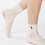 Woman wearing a white ankle grip sock with a tulip motif embroidered on the ankle side, made for pilates, barre, yoga, and beyond. 