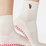 Woman wearing a white ankle grip sock with a tulip motif embroidered on the ankle side, made for pilates, barre, yoga, and beyond. 